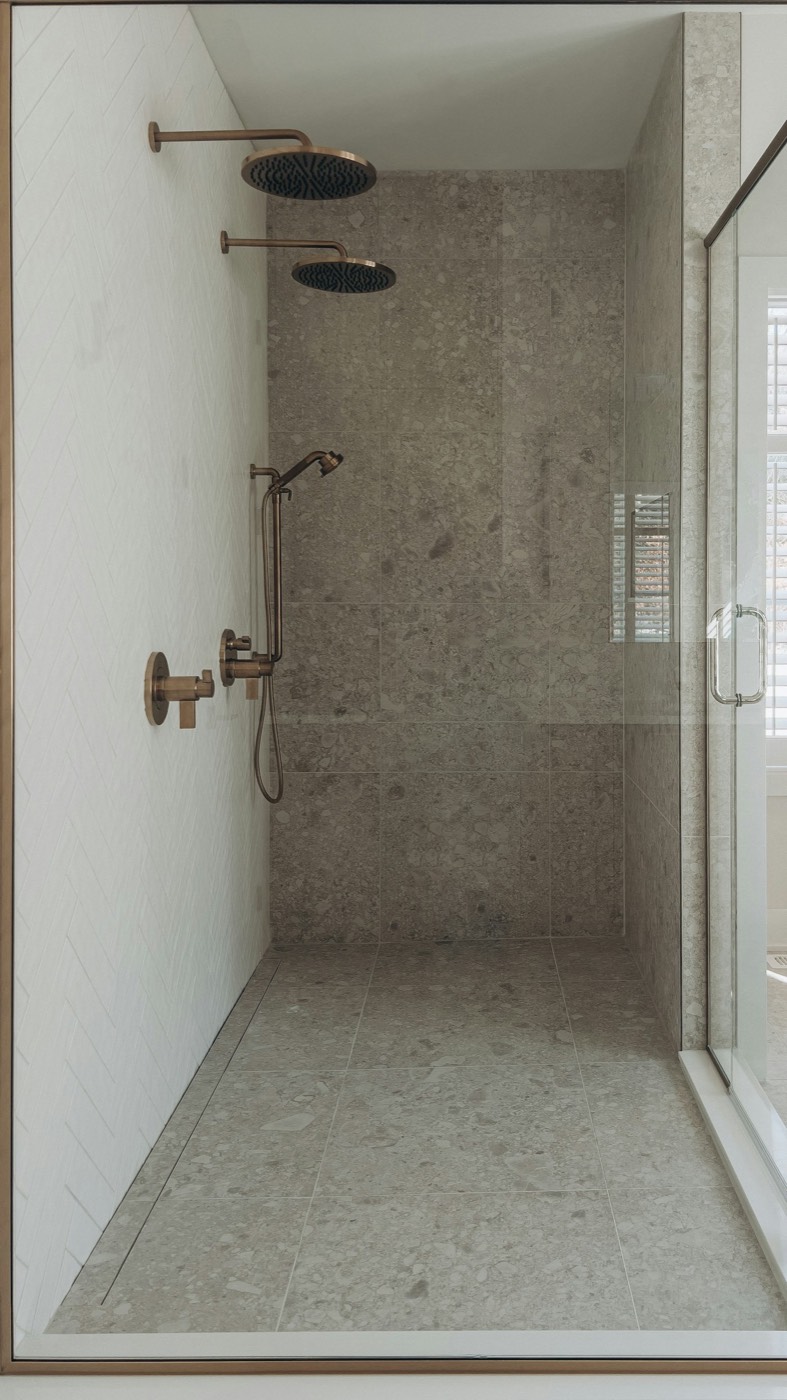 A walk-in shower with a stone-look wall and brass fixtures