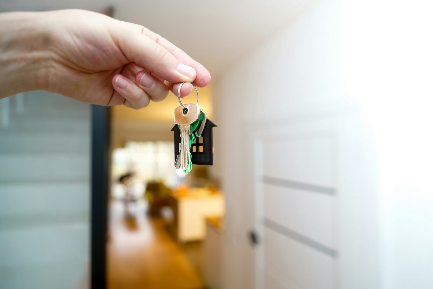 A hand holding a set of house keys in a bright hallway