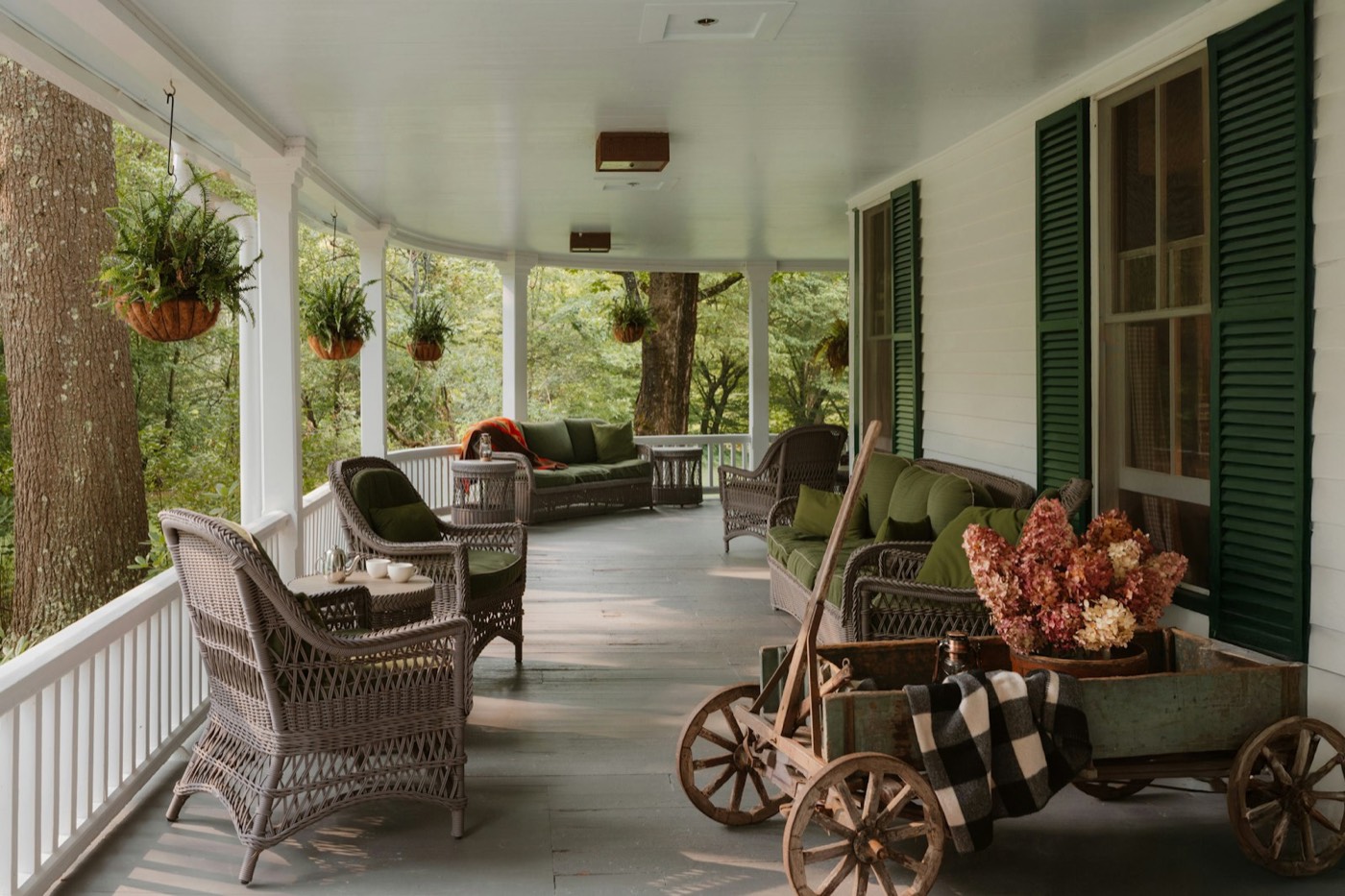 The covered front porch of a house, with wicker chairs and potted plants